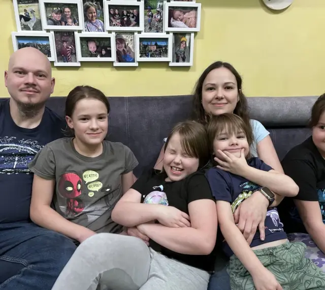 Szczęśliwa rodzina wielodzietna siedzi na kanapie. Rodzice i pięcioro dzieci uśmiechają się do aparatu.