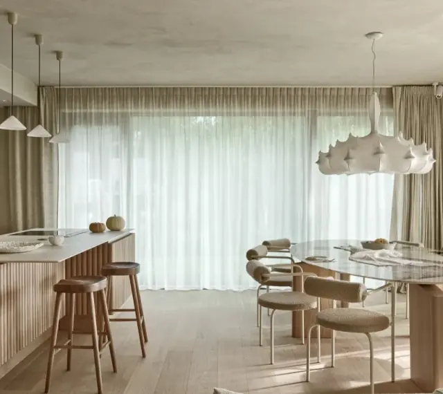 Nowoczesna kuchnia z wyspą i jadalnią. Wnętrze rozświetla designerska lampa wisząca, a całość dopełnia podwieszany sufit.