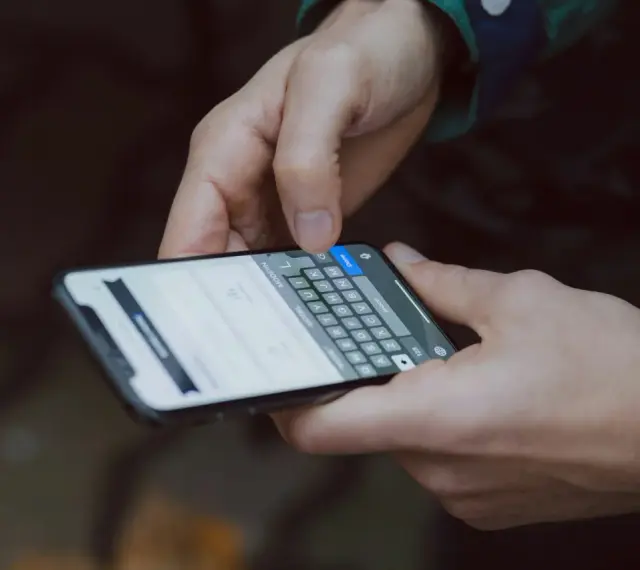 Dłonie trzymają smartfon z klawiaturą. Dowiedz się, jak wydrukować zdjęcie z telefonu, by zachować wspomnienia.