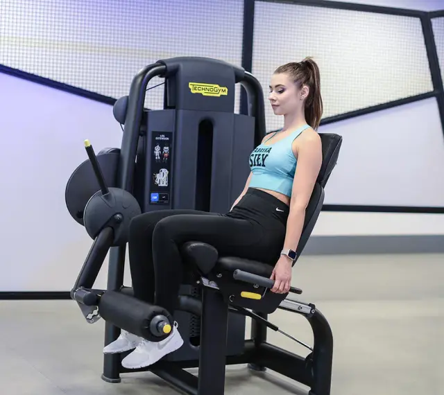 Kobieta wykonuje wyprosty nóg na maszynie Technogym, ćwicząc mięśnie czworogłowe uda.