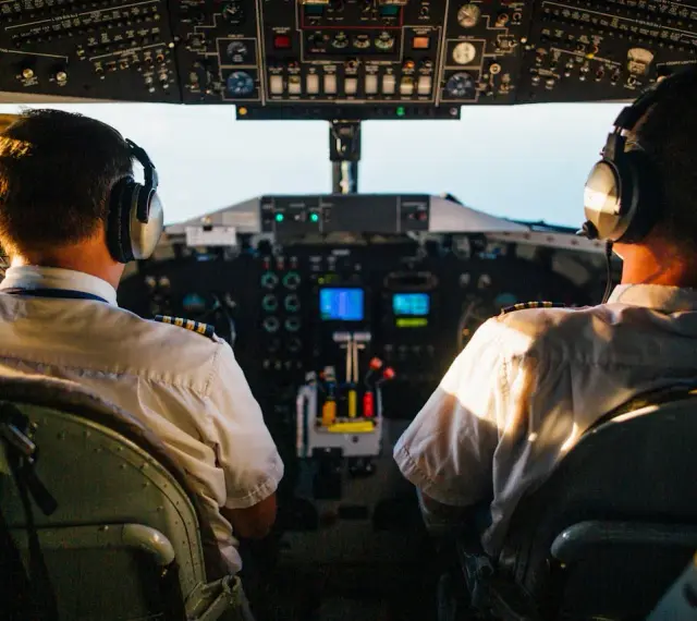 Dwóch pilotów samolotu w słuchawkach na tle kokpitu.