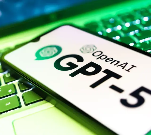 Ekran smartfona z logo OpenAI i napisem GPT-5 leży na podświetlanej zielonej klawiaturze.