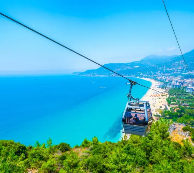 Kolejka linowa nad turkusowym morzem i plażą w Alanyi. Widok z góry na miasto i wybrzeże. Czy Alanya jest bezpieczna? Tak, wygląda na spokojną i piękną.