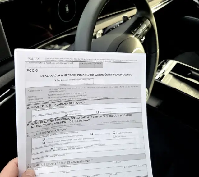 Deklaracja PCC-3, dokument dotyczący podatku od kupna samochodu, leży na desce rozdzielczej auta.