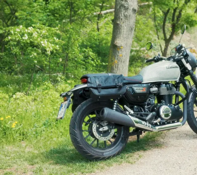 Stojący na poboczu, w otoczeniu zieleni, motocykl Honda GB350 z sakwami gotowy na podróż.