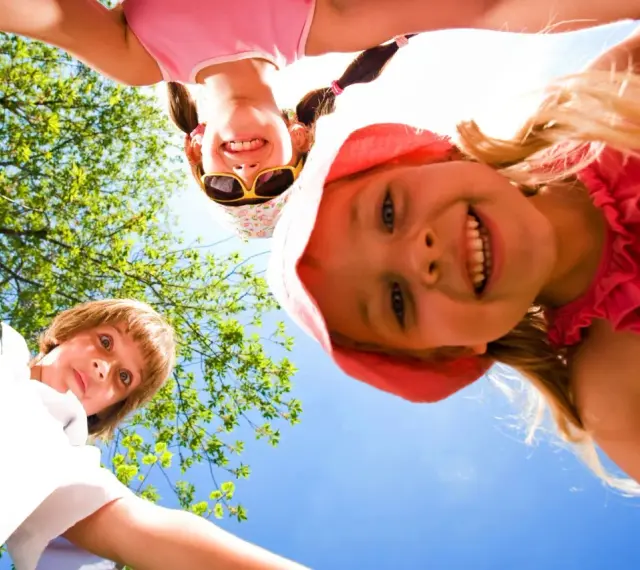 Trois enfants souriants, vus d'en bas, profitent d'une journée ensoleillée lors d'un camp sportif.