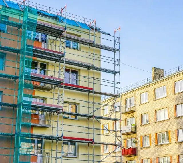 Budynek w remoncie, rusztowania i siatka ochronna. Balkony we wspólnocie mieszkaniowej czekają na odnowienie.