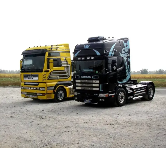 Dwa ciągniki siodłowe: żółty MAN i czarna Scania z grafiką. Różne rodzaje naczep czekają na załadunek.
