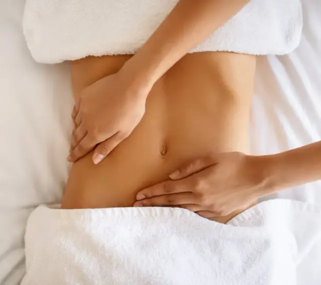 Hände massieren sanft den Bauch einer Frau. Manche empfinden Lymphdrainage als schmerzhaft, doch hier scheint es eine wohltuende Behandlung zu sein.