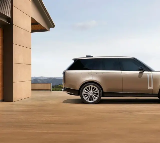 Elegancki Range Rover w kolorze piaskowym, zaparkowany przed nowoczesnym domem z drewnianymi drzwiami. Sprawdź range rover cena!