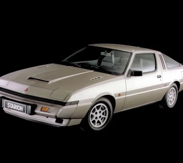 Klasyczny Mitsubishi Starion w kolorze szampańskim, z charakterystycznym wlotem powietrza na masce i sportowym nadwoziem coupe.