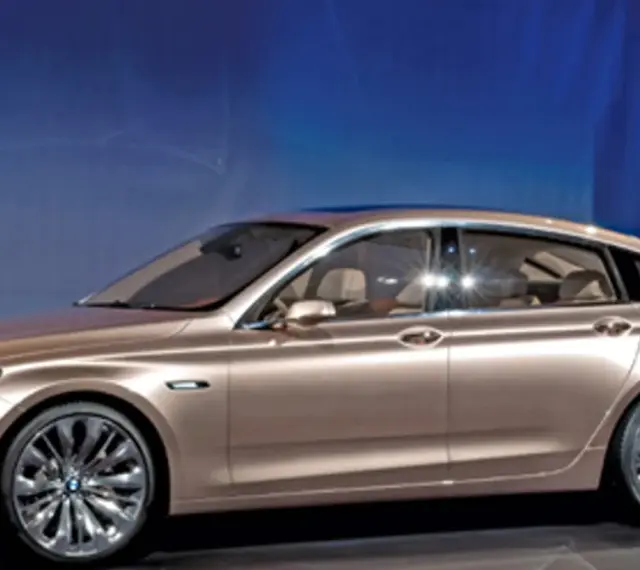 Eleganckie, złote bmw gt z przyciemnianymi szybami i chromowanymi felgami stoi na tle niebieskiej ściany.