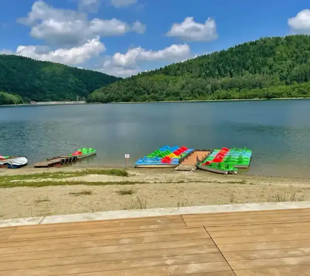 Kolorowe rowery wodne i kajaki czekają na plaży nad górskim jeziorem.