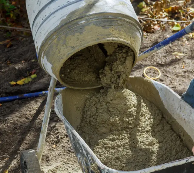 Betoniarka wylewa świeży beton do taczki. Właściwa ilość cementu na 1 m3 betonu jest kluczowa dla jego wytrzymałości.