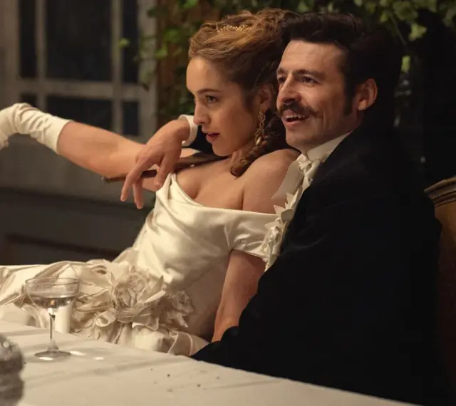 Elegancka para przy stole, zapowiedź nowych produkcji Netflix. Kobieta w białej sukni z rękawiczkami, mężczyzna w czarnym fraku.