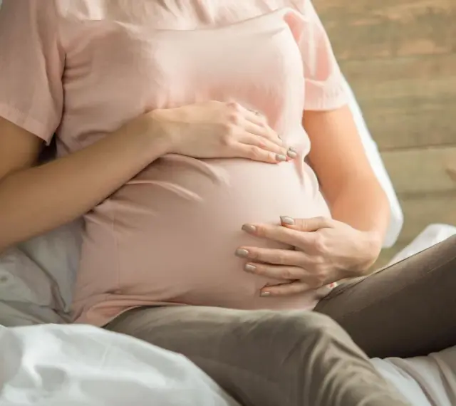 Kobieta w ciąży z dłońmi na brzuchu, martwiąca się o niskie erytrocyty w ciąży.
