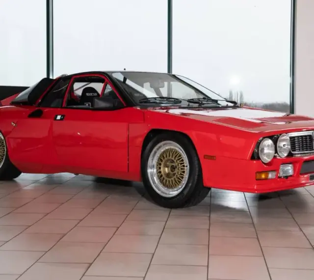 Czerwona Lancia 037 z czarnym spojlerem i złotymi felgami, gotowa do rajdu.