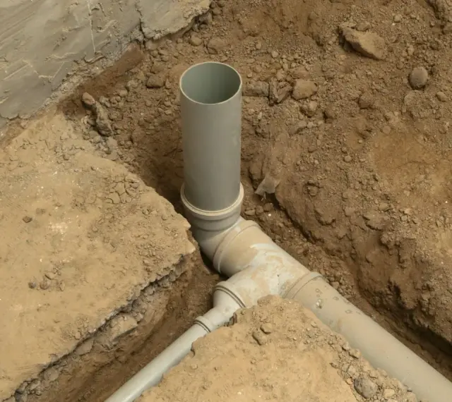 Wykop pod kanalizację z szarymi rurami PVC, częściowo zasypany ziemią.
