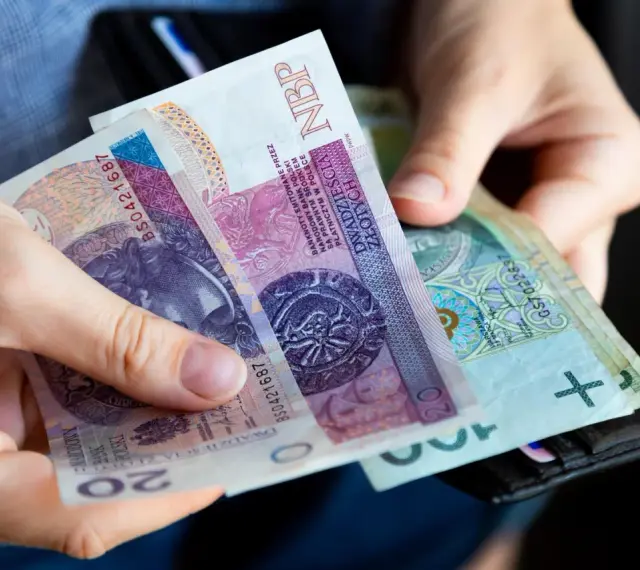 Dłonie trzymają polskie banknoty 20 zł i 100 zł. Wkrótce może pojawić się ryczałt energetyczny.