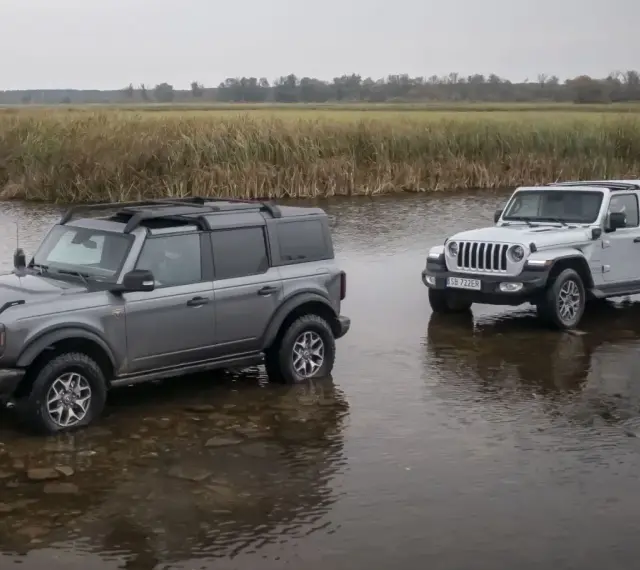 Szary Ford Bronco i biały Jeep SUV stoją w płytkiej wodzie, gotowe na przygodę.