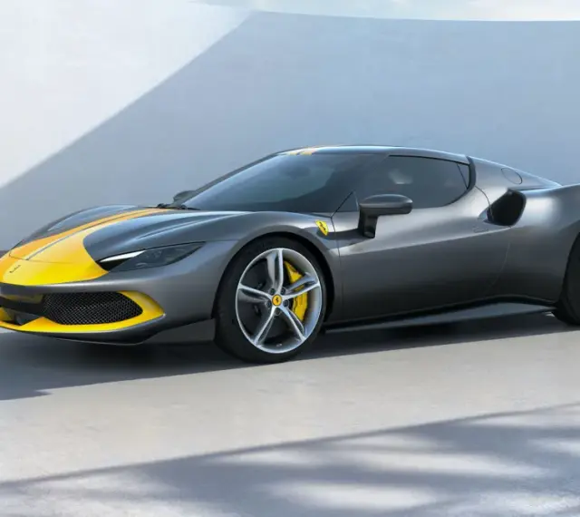 Szary Ferrari 296 GTB z żółtymi pasami na masce i dachu, stojący na betonowej posadzce.