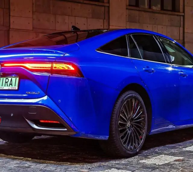 Niebieska Toyota Mirai z podświetlonymi światłami tylnymi stoi na brukowanej ulicy nocą.