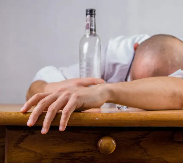 Mężczyzna śpi na stole, obok pusta butelka. Połączenie kofeiny i alkoholu doprowadziło do wyczerpania.