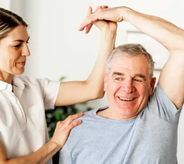 Physiotherapeutin unterstützt Mann bei Übungen zur Wiederherstellung der Beweglichkeit nach Schlaganfall. Verordnung Physiotherapie nach Schlaganfall wird umgesetzt.