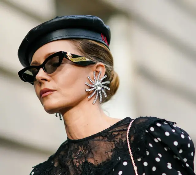 Kobieta w czarnym beretce i okularach przeciwsłonecznych, z dużą, błyszczącą kolczykiem. Czy grochy są modne? Ta stylizacja sugeruje, że tak!