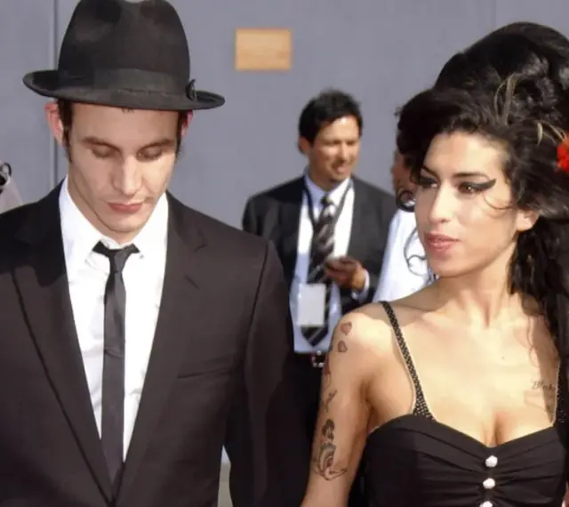 Blake Fielder-Civil w czarnym garniturze i kapeluszu obok Amy Winehouse z czerwoną różą we włosach.
