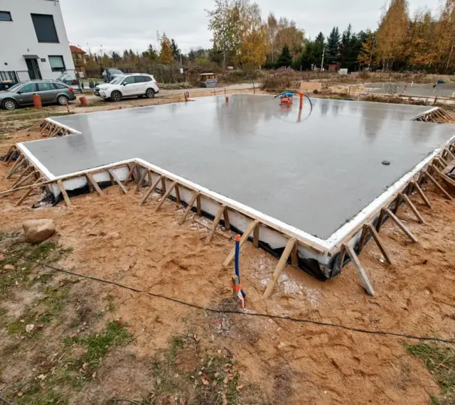 Świeżo wylany beton na budowie. To solidne, najtańsze fundamenty pod przyszły dom, otoczone drewnianym szalunkiem.