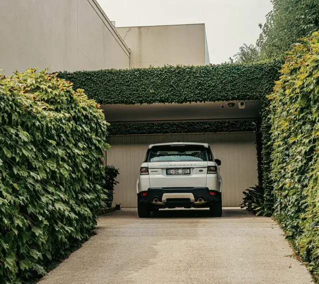 Biały Range Rover wjeżdża na podjazd otoczony bujną zielenią. Naturalna ściana z bluszczu to świetna alternatywa co zamiast kostki na podjazd.