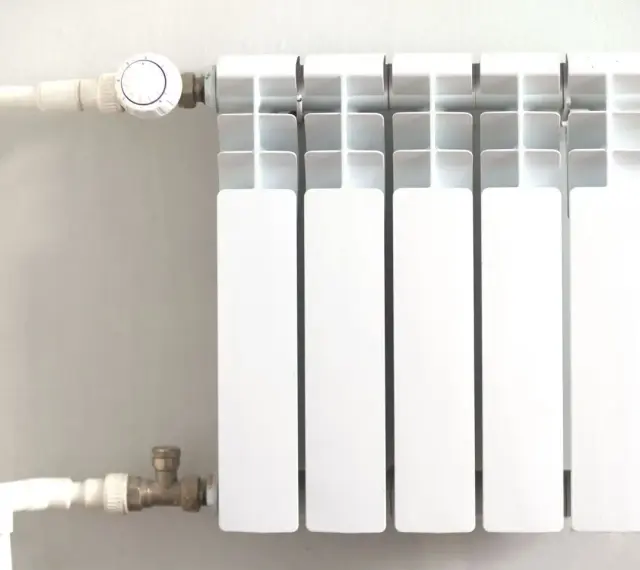 Biały grzejnik z termostatem, podłączony do instalacji rurowej. To efektywne ogrzewanie etażowe, które zapewnia komfort cieplny.