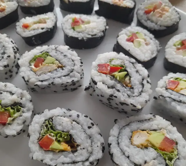 Pyszne domowe sushi z kurczakiem, awokado i warzywami, posypane czarnym sezamem.