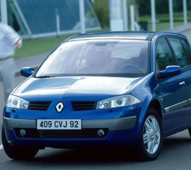 Niebieski Renault Megane 2 na drodze, z parą ludzi w tle.