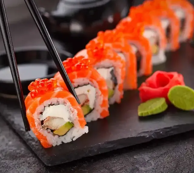 Chopsticks podnoszą kawałek sushi z łososiem i ikrą. Czy sushi jest lekkostrawne? Zależy od składników, ale ten wygląda apetycznie.