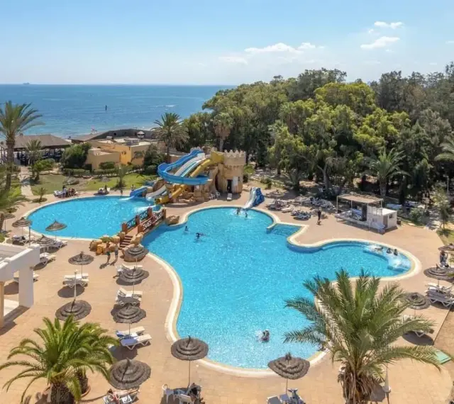 Hotel Marhaba Royal Salem kusi basenem z wodnymi zjeżdżalniami i palmami, w tle morze.