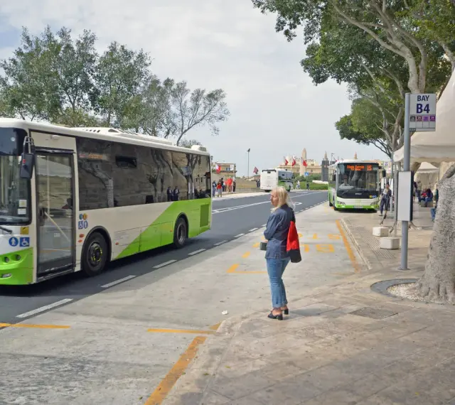 Kobieta czeka na autobus na Malcie. W tle widać autobusy, w tym jeden jadący w kierunku lotniska.