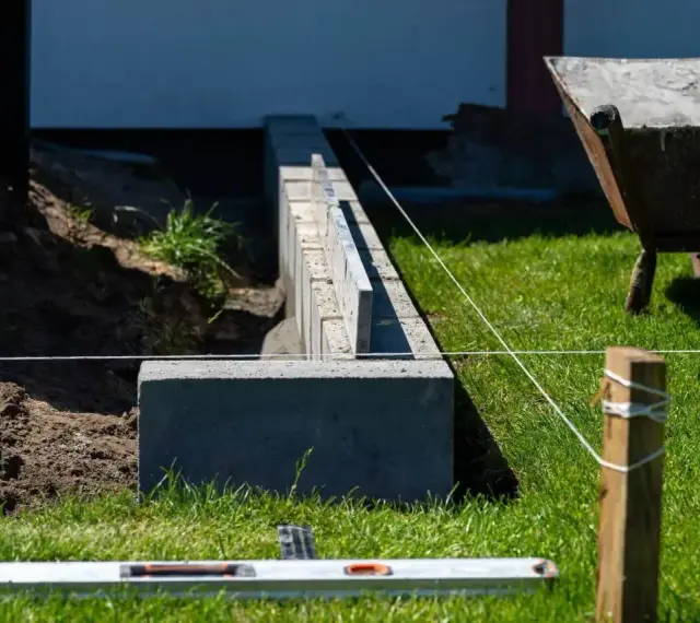Budowa fundamentu pod ogrodzenie. Betonowe bloczki tworzą solidną podstawę, a niwelacyjna linka wyznacza precyzyjną linię.