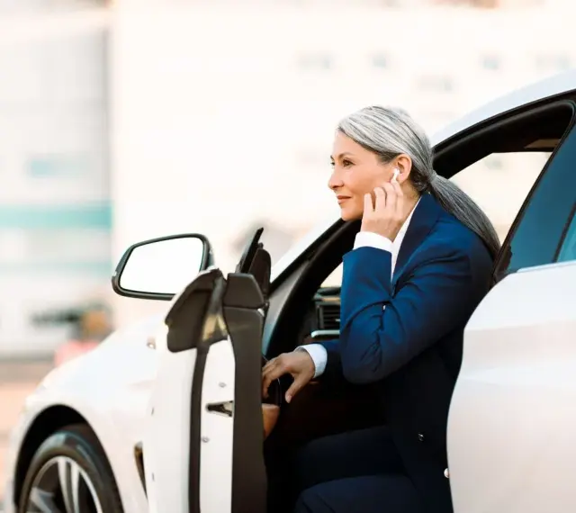 Elegancka kobieta w garniturze wsiada do białego auta. To jej auto na abonament, idealne do biznesowych podróży.