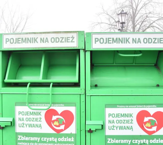Dwa zielone kontenery na odzież używaną, z napisem "POJEMNIK NA ODZIEŻ UŻYWANĄ" i sercem z symbolami recyklingu.