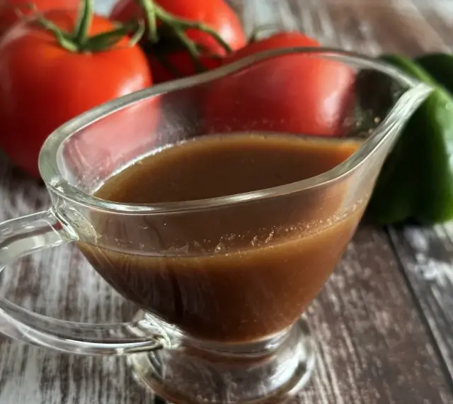 Sos balsamiczny w sosjerce, w tle pomidory i zielona papryka. Idealny do sałatek i mięs.