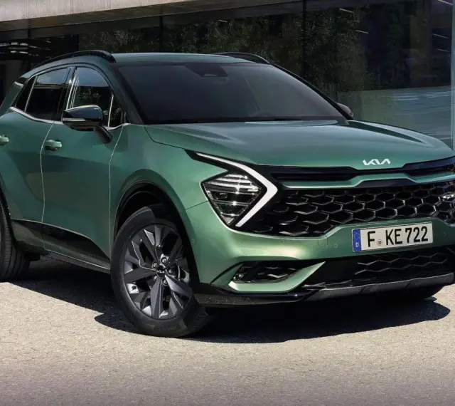 Nowy zielony Kia Sportage 1.6 benzyna z nowoczesnym designem, zaparkowany przed budynkiem.