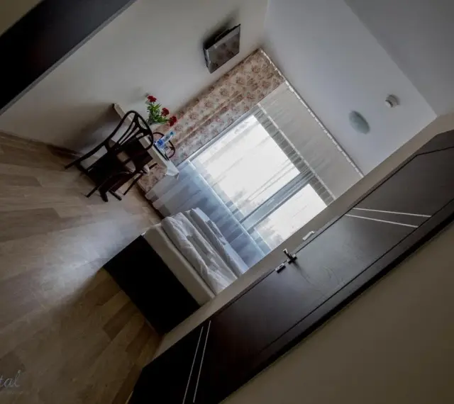 Pokój w hotelu i restauracji Crystal: łóżko, stolik z krzesłami i kwiatami, okno z zasłonami.