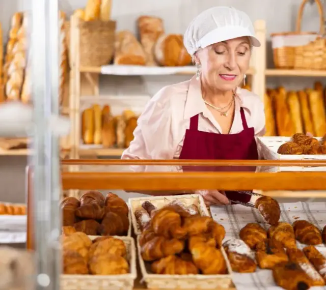 Starsza pani piekarz z uśmiechem układa świeże croissanty. To ulga dla pracujących seniorów, którzy wciąż mają pasję.
