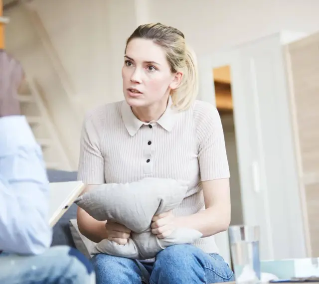 Kobieta w trakcie sesji u psychiatry, ściska poduszkę, szukając ukojenia.