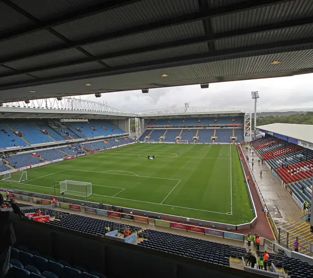 Widok na murawę i trybuny stadionu Ewood Park. Puste miejsca na niebieskich i czerwonych siedzeniach.
