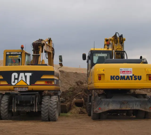 Dwie żółte koparko-ładowarki, CAT i Komatsu, stoją na placu budowy. Czy koparko ładowarka musi być zarejestrowana?