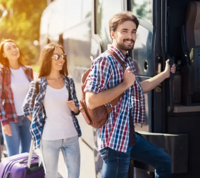 Grupa młodych ludzi z plecakami i walizką wsiada do autobusu, gotowa na wycieczki fakultatywne.