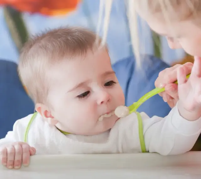 Mama karmi dziecko łyżeczką do karmienia niemowląt. Maluch z zaciekawieniem patrzy na jedzenie.